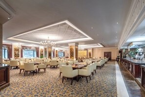 A spacious hotel dining area with multiple tables and chairs, a chandelier, and a patterned carpet. - Evergrande World MICE Center (Jintang)