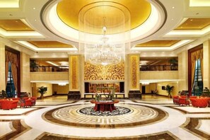 Un lobby imponente con una gran araña central, un piso con patrón circular y una zona de estar con sofás rojos.