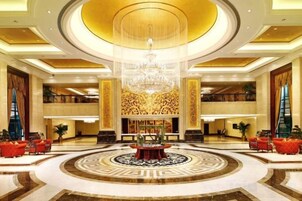 Un lobby imponente con una gran araña central, un piso con patrón circular y una zona de estar con sofás rojos.