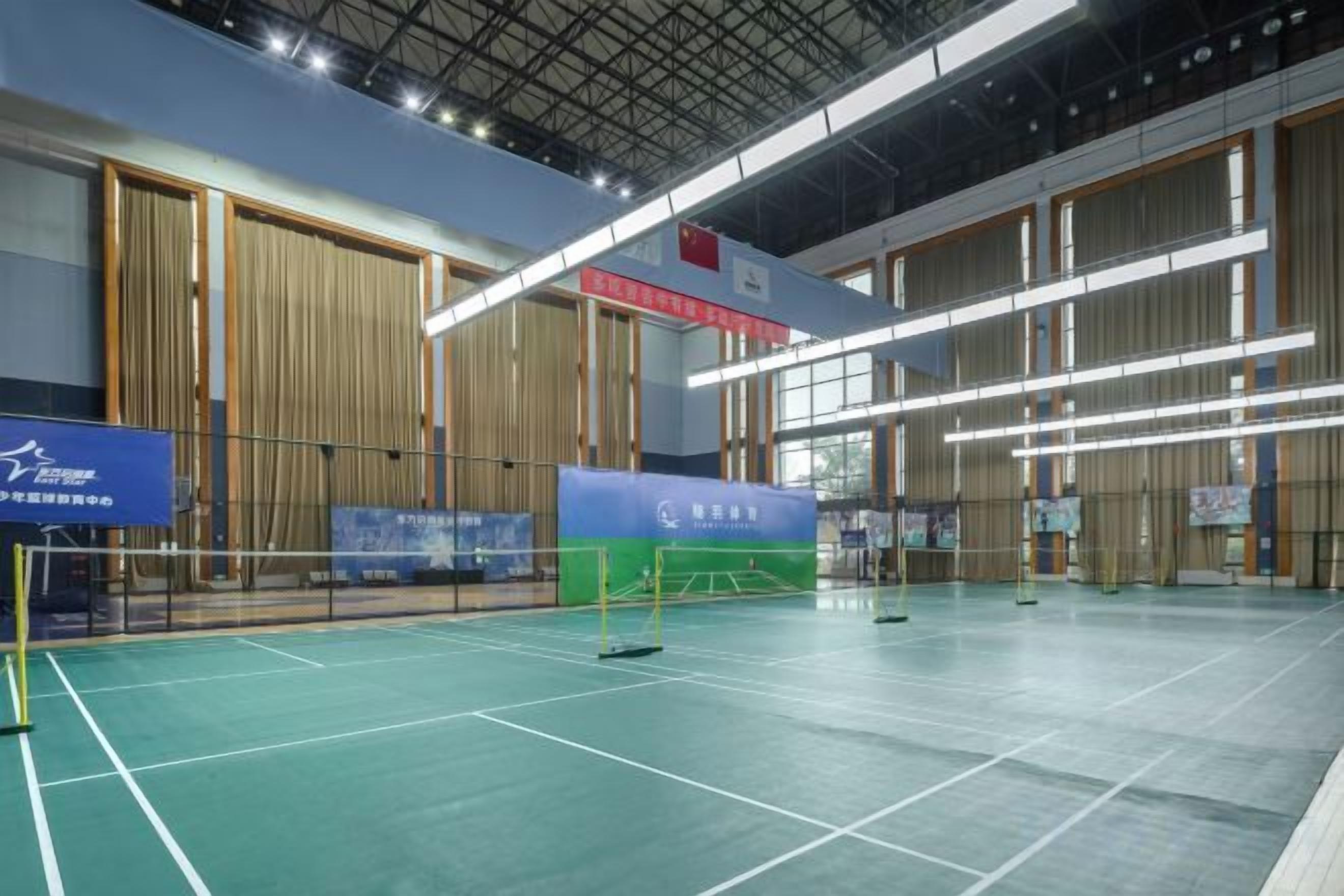 Una cancha de bádminton en interior con una red, paredes de madera e imágenes publicitarias.