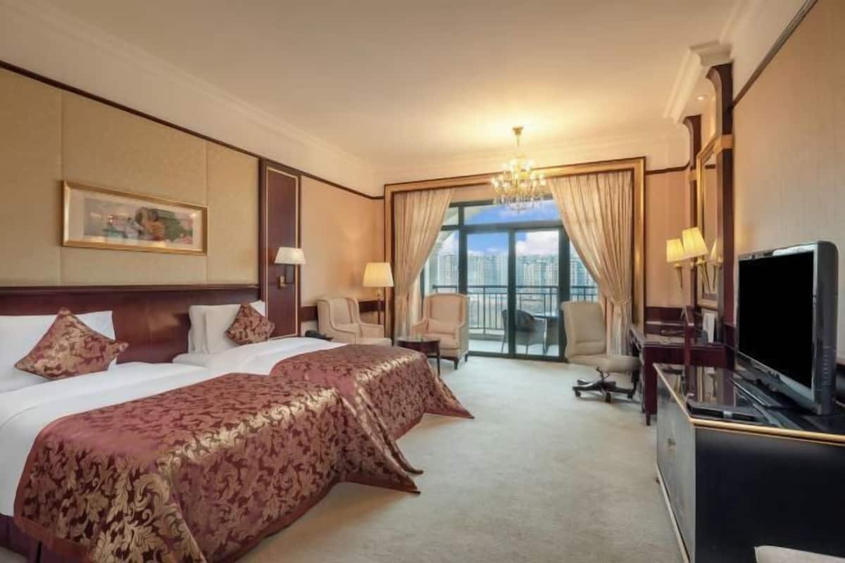 A hotel room with two beds, a television, a desk, and a large window with a city view.