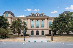 Un grand bâtiment historique à la façade symétrique, doté de larges fenêtres en arc de cercle et d’une entrée centrale.