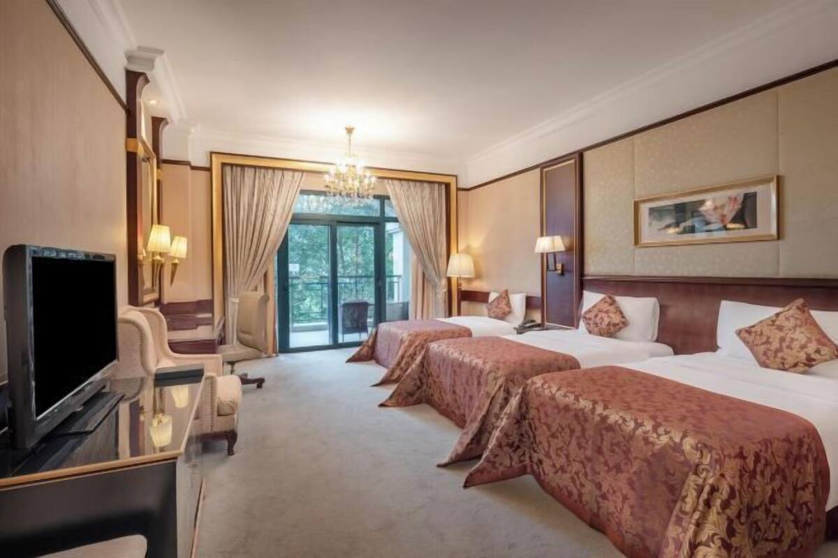 A hotel room with a TV, two beds, a desk, and a large window.