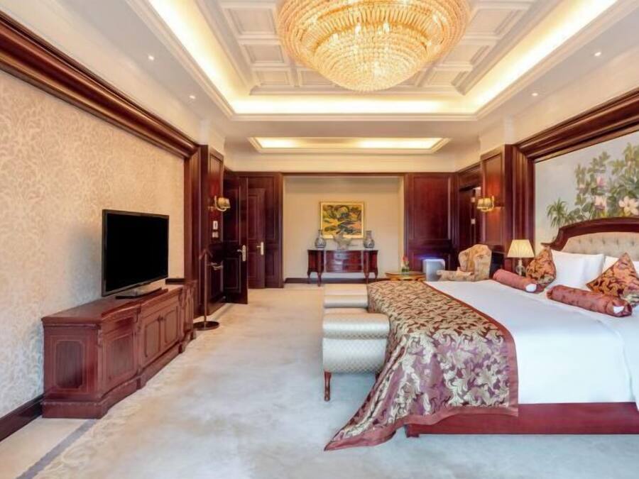 A spacious hotel room with a large bed, a television, and a chandelier.