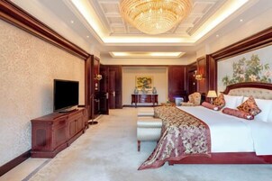Una habitación de hotel amplia con una cama grande, televisión y una araña.