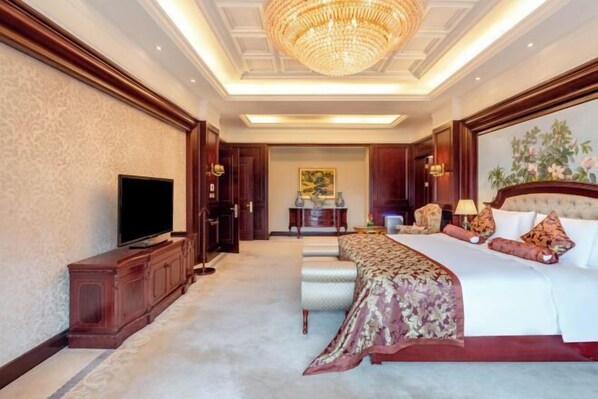 A spacious hotel room with a large bed, a television, and a chandelier.