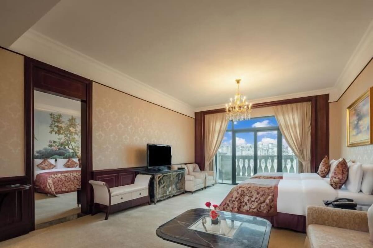 A hotel room with a large bed, a television, a sofa, a coffee table, and a balcony with a city view.