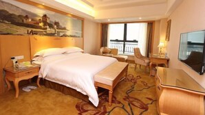 A hotel room with a large bed, a desk, a chair, a TV, and a painting on the wall. - Vienna International Hotel (Shenzhen Xiashuijing Metro Station) (Shenzhen)