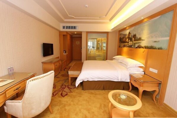 Une chambre d’hôtel avec un lit, un bureau, une chaise, une petite table et un tableau au mur.