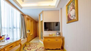 A hotel room with a large window, a flat-screen TV, a wooden desk, a small dresser, and a floral carpet. - Vienna International Hotel (Shenzhen Xiashuijing Metro Station) (Shenzhen)