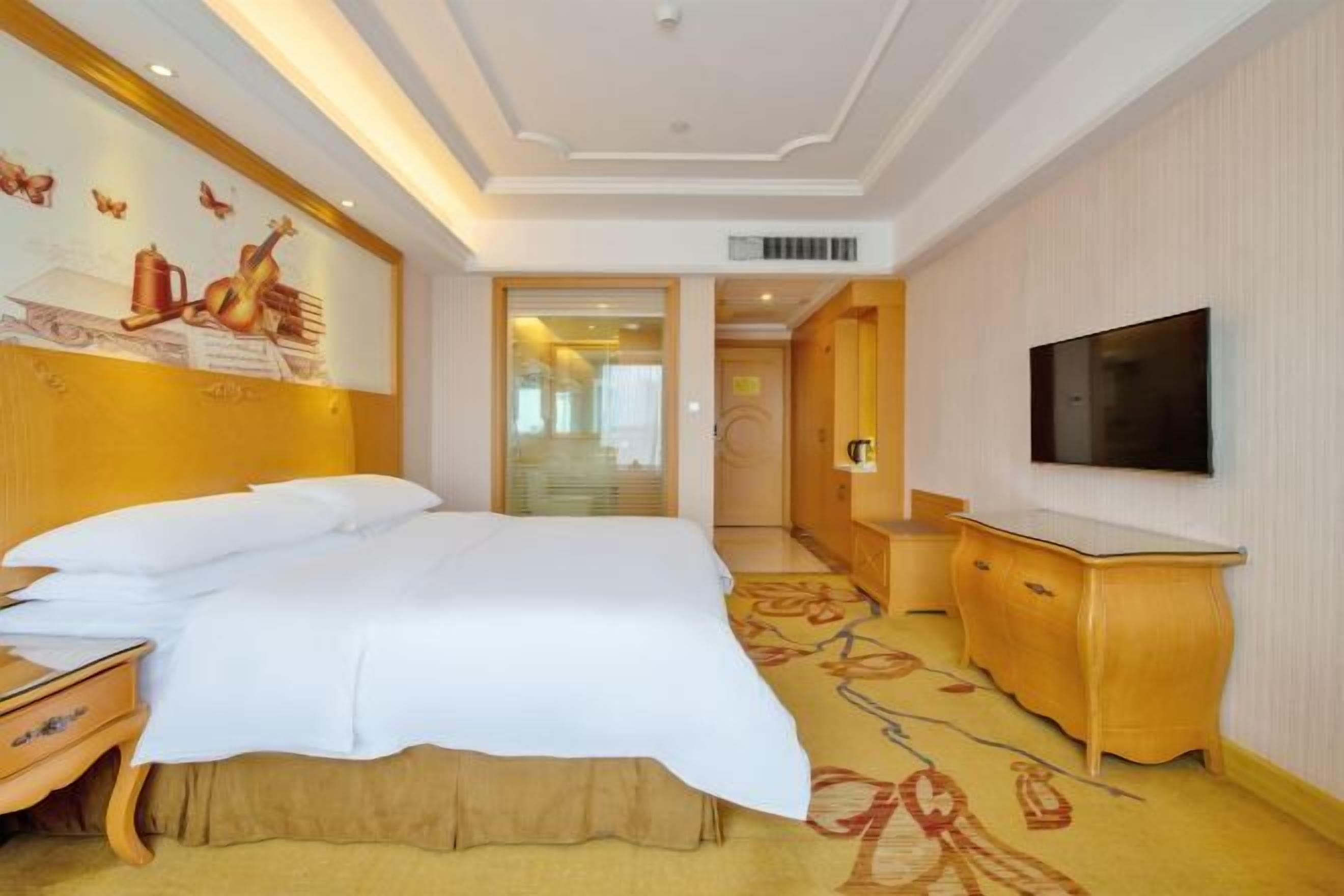 A hotel room with a bed, bedside table, TV, and a wall with a mural.