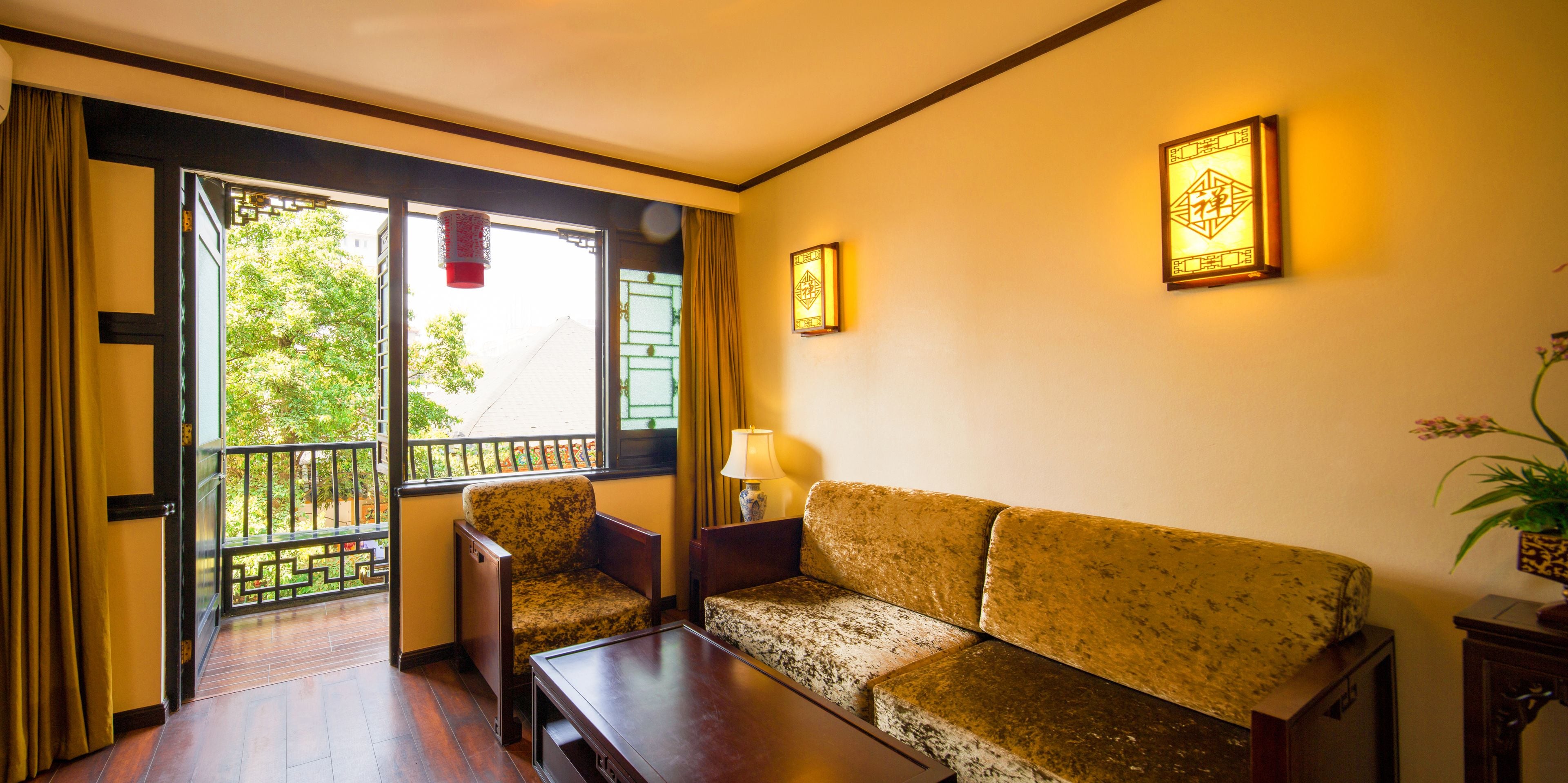 Habitación con sofá, una silla, una mesa y ventana con vista a áreas verdes.