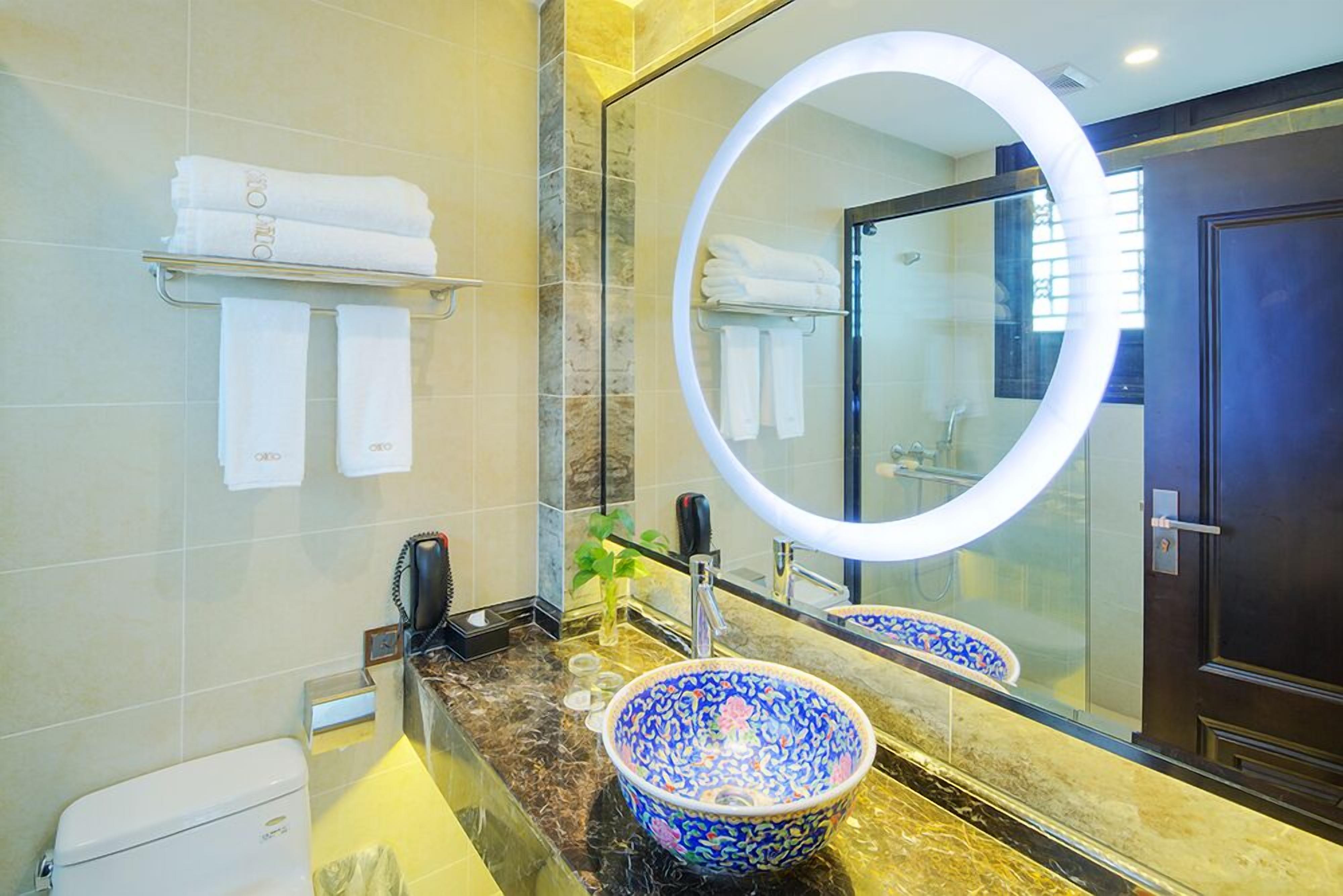 Un baño con encimera de mármol, lavamanos de porcelana con diseño azul y blanco, espejo redondo y toallero con toallas dobladas.