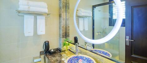 Un baño con encimera de mármol, lavamanos de porcelana con diseño azul y blanco, espejo redondo y toallero con toallas dobladas.