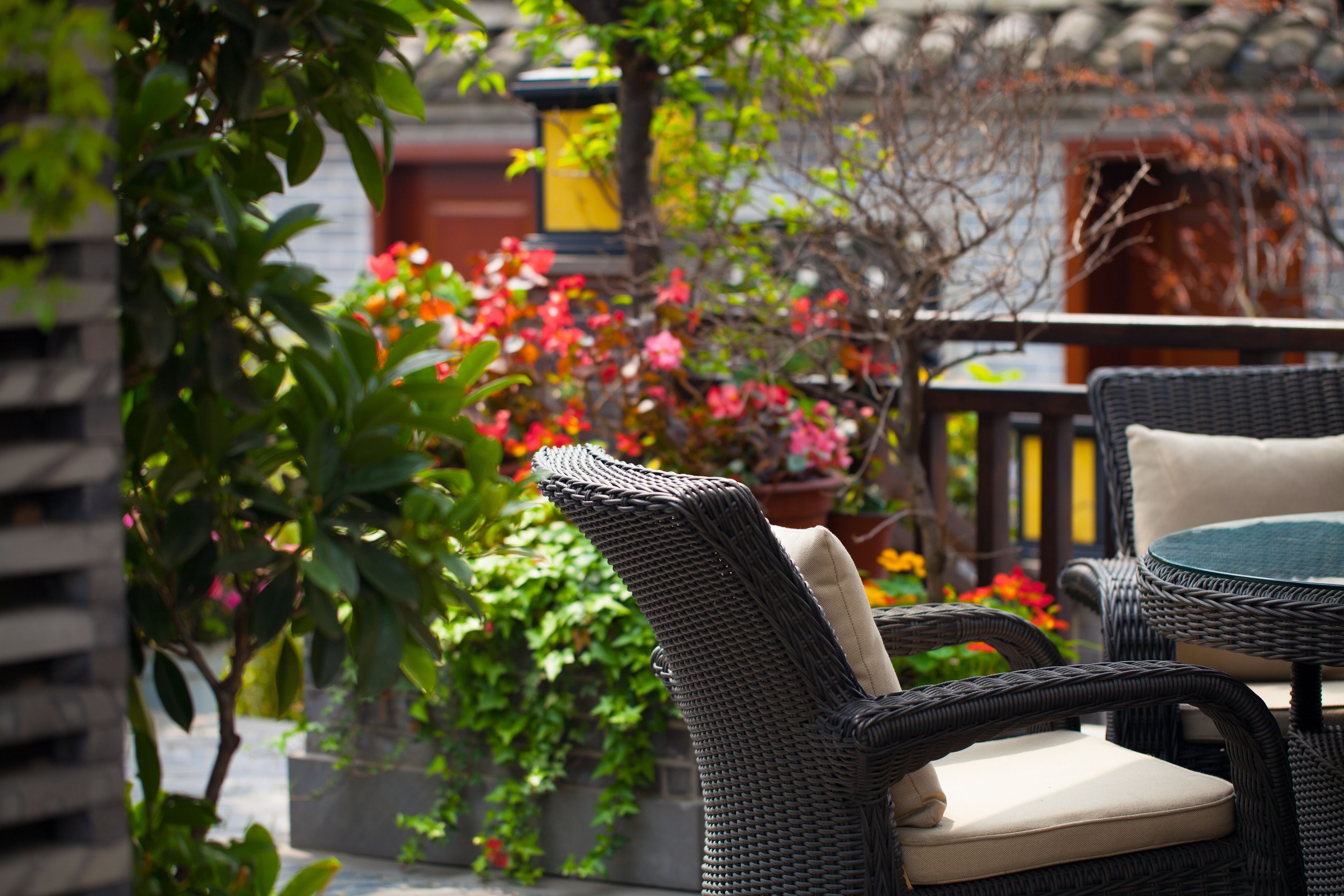 A wicker outdoor seating area with cushioned chairs and a round table, surrounded by lush greenery and vibrant flowers.