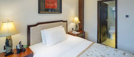 A hotel room with a bed, bedside lamps, a framed picture on the wall, a nightstand, and a door leading to the bathroom.