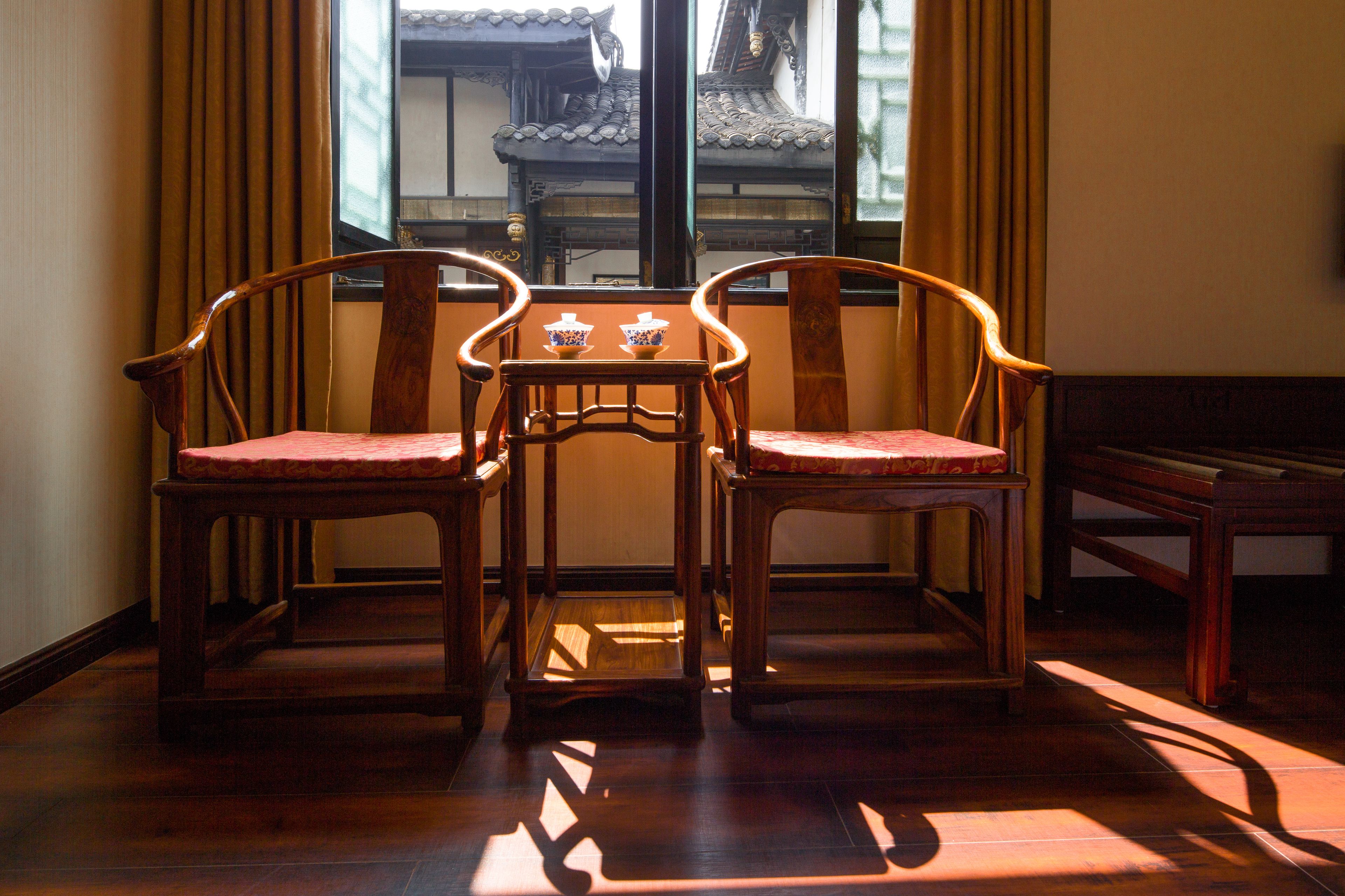 A traditional wooden table with two chairs in a room with wooden flooring and a window with curtains.