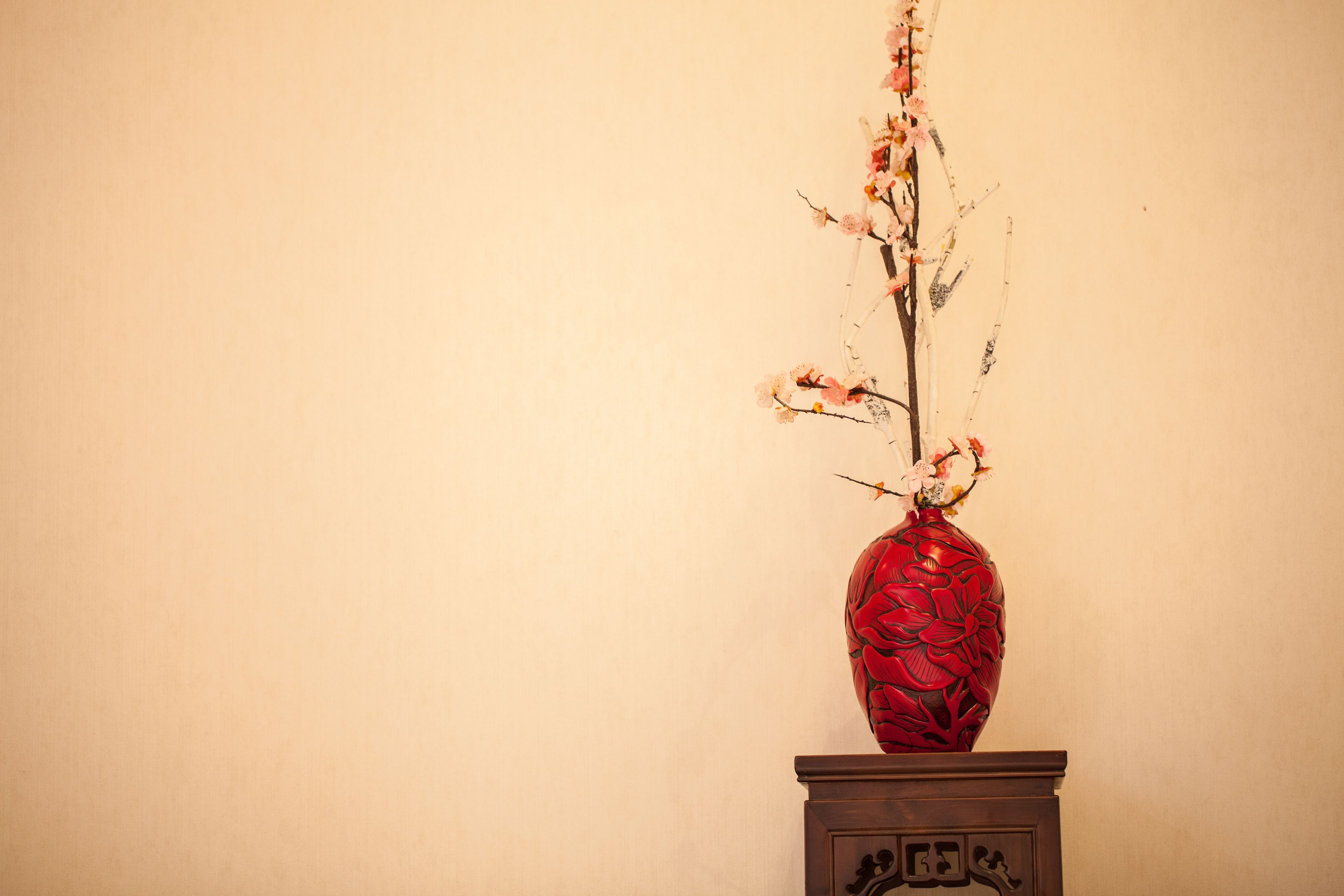 A red vase with floral patterns on a wooden pedestal against a plain wall.