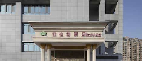A hotel entrance with a sign in a foreign language, a classical architectural style with columns, and a clear sky.
