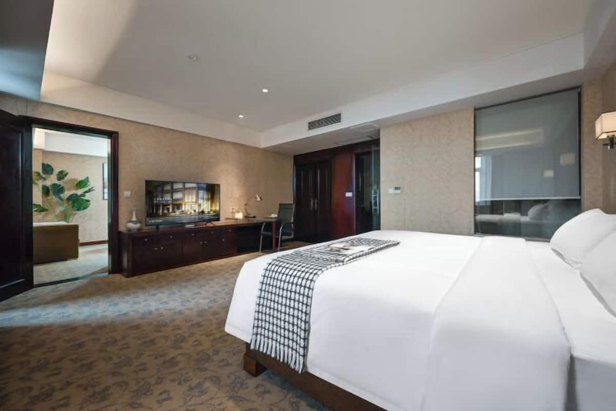 A hotel room with a large bed, a desk, a television, and a sliding door leading to a balcony.