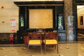 A lobby with a reception desk, two wooden chairs with yellow cushions, a decorative wall, and a fire extinguisher. - Agile Hotel (Zhongshan)