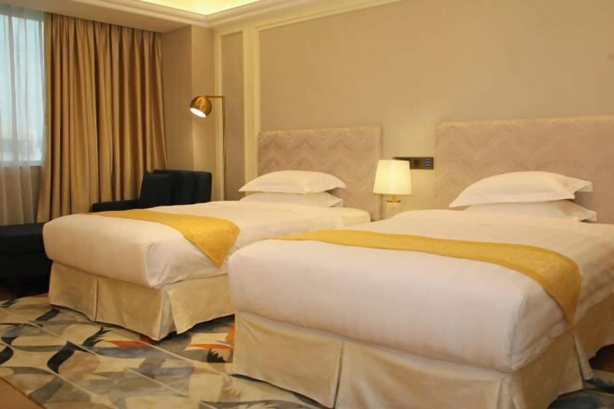 A hotel room with two beds, a desk, a chair, and a lamp.