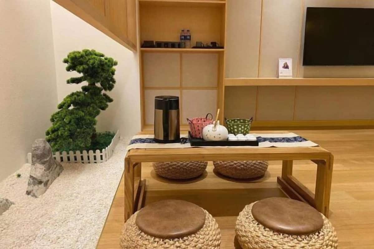 A room with a wooden table, woven stools, a small potted plant, a decorative stone, and a television on the wall.