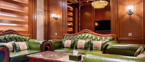 A green leather sofa set with a marble coffee table, wooden paneling, and wall sconces.