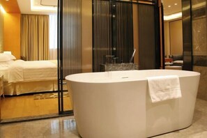 A modern bathroom with a large oval bathtub, a glass shower enclosure, and a bed with white linens. - Agile Hotel (Zhongshan)