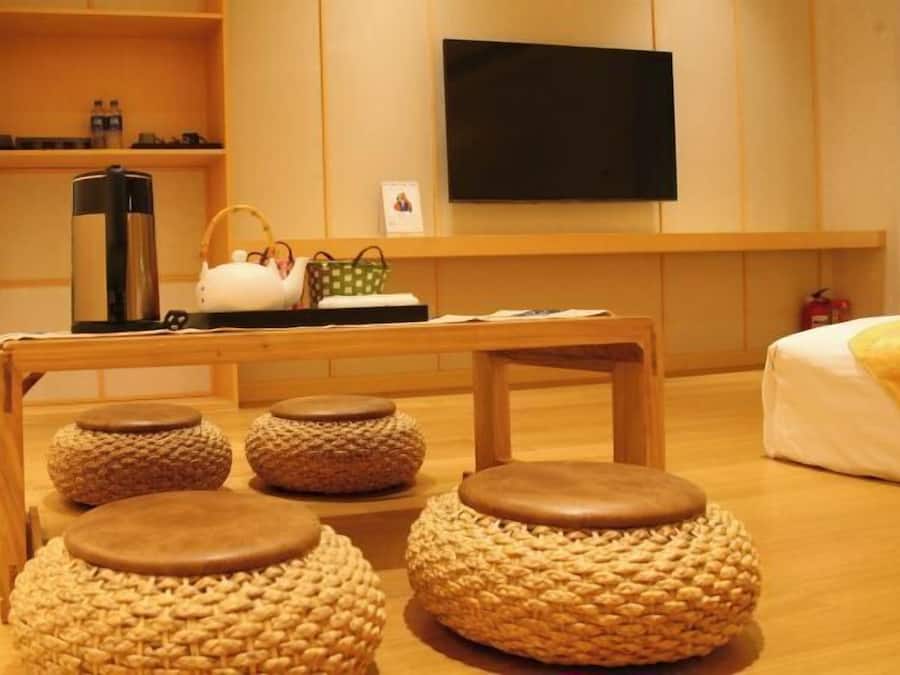 Habitación de hotel con una mesa de madera, cuatro taburetes tejidos, un televisor y una cama con manta amarilla.