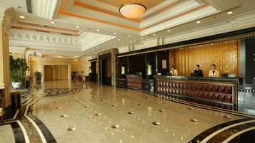 A hotel lobby with a reception desk, a large chandelier, and a marble floor.