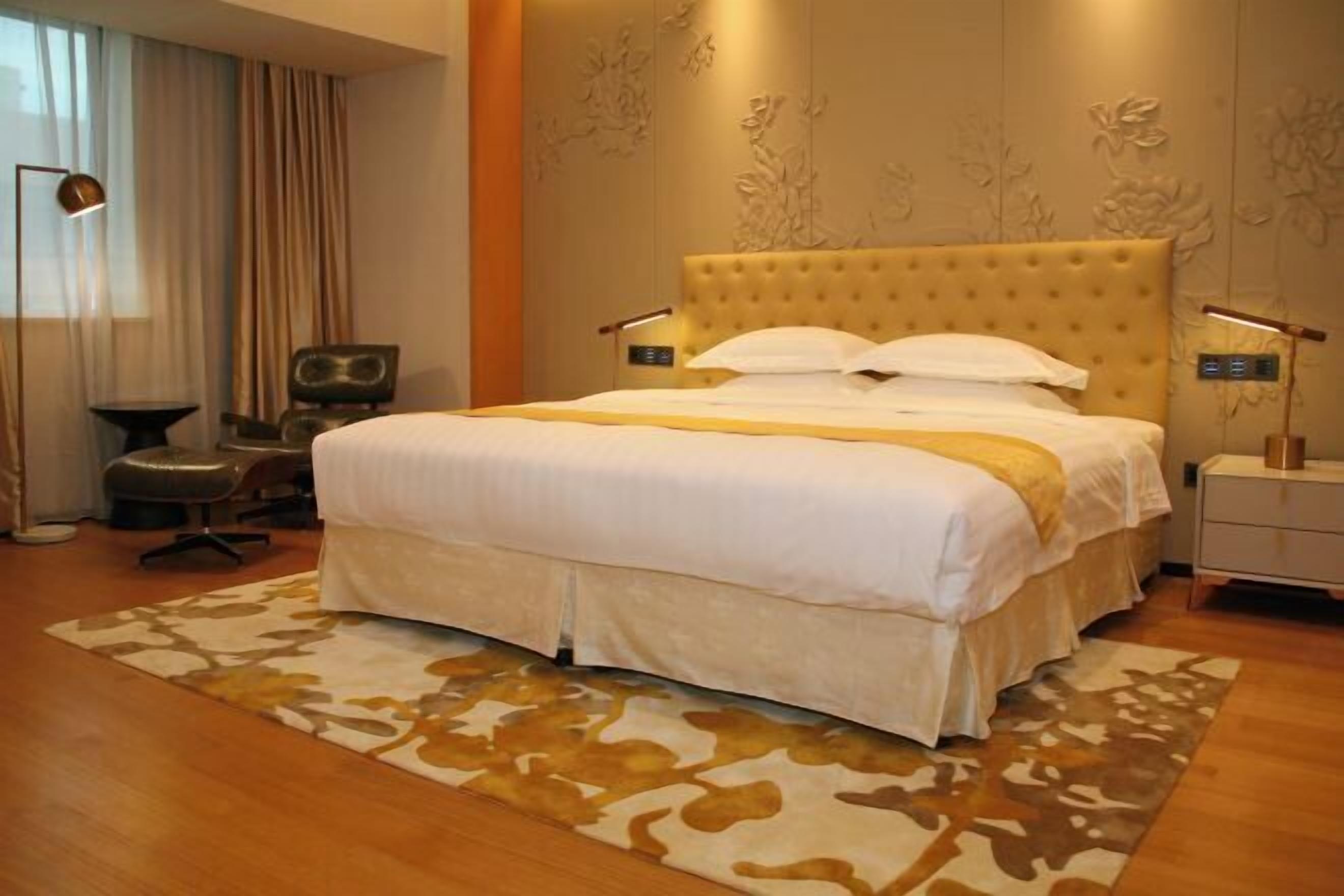 A hotel room with a large bed, a desk, a chair, and a lamp.