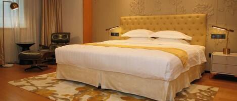A hotel room with a large bed, a desk, a chair, and a lamp.