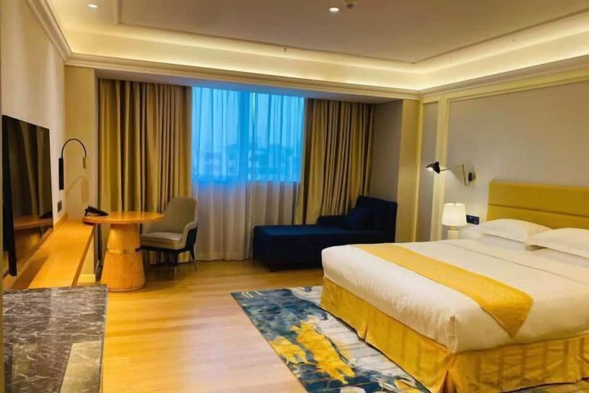 A hotel room with a bed, a desk, a chair, a small table, and a window with curtains.