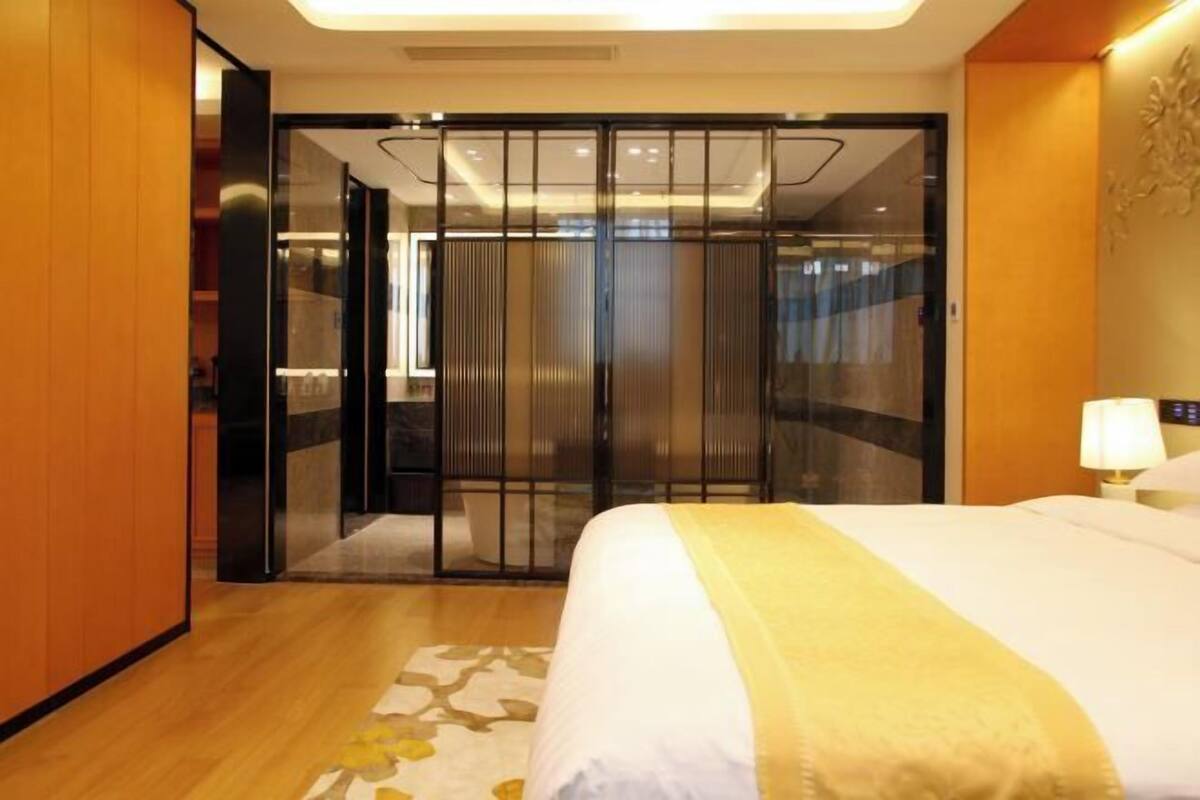 A hotel room with a bed, a nightstand, a lamp, a sliding door, and a wooden floor.