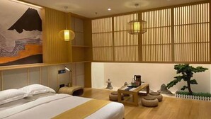 A hotel room with a bed, a desk, a lamp, a wall-mounted shelf, and a decorative wall piece. - Agile Hotel (Zhongshan)