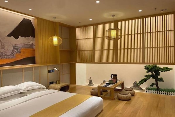 A hotel room with a bed, a desk, a lamp, a wall-mounted shelf, and a decorative wall piece.
