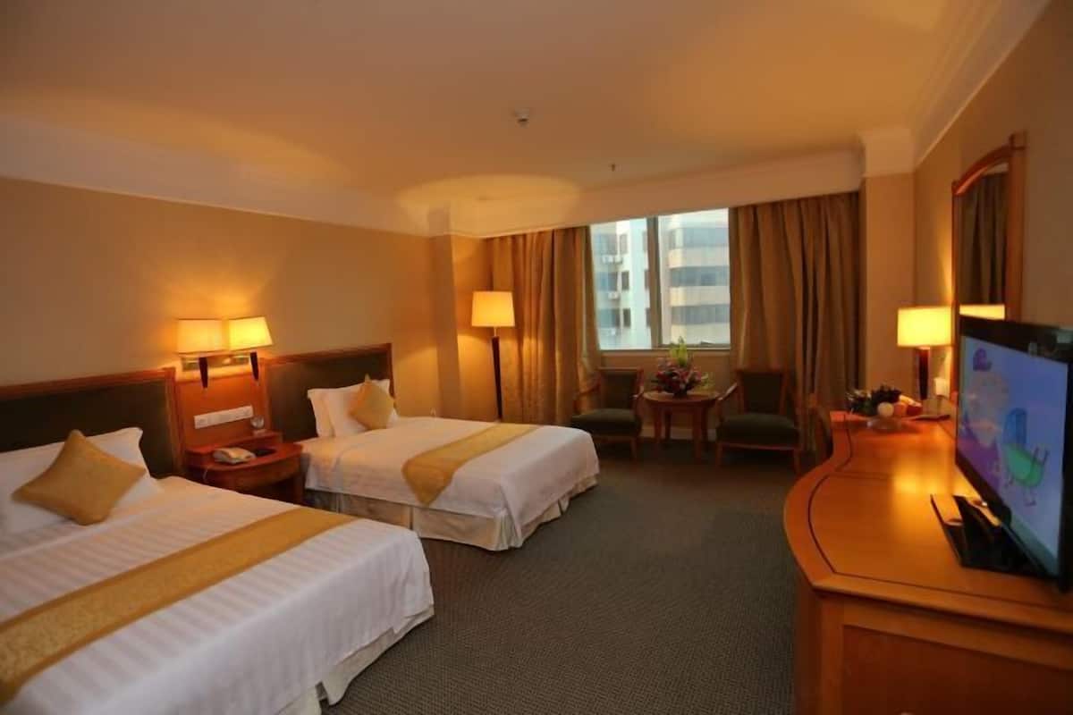 A hotel room with two beds, a desk, a television, and a window with curtains.