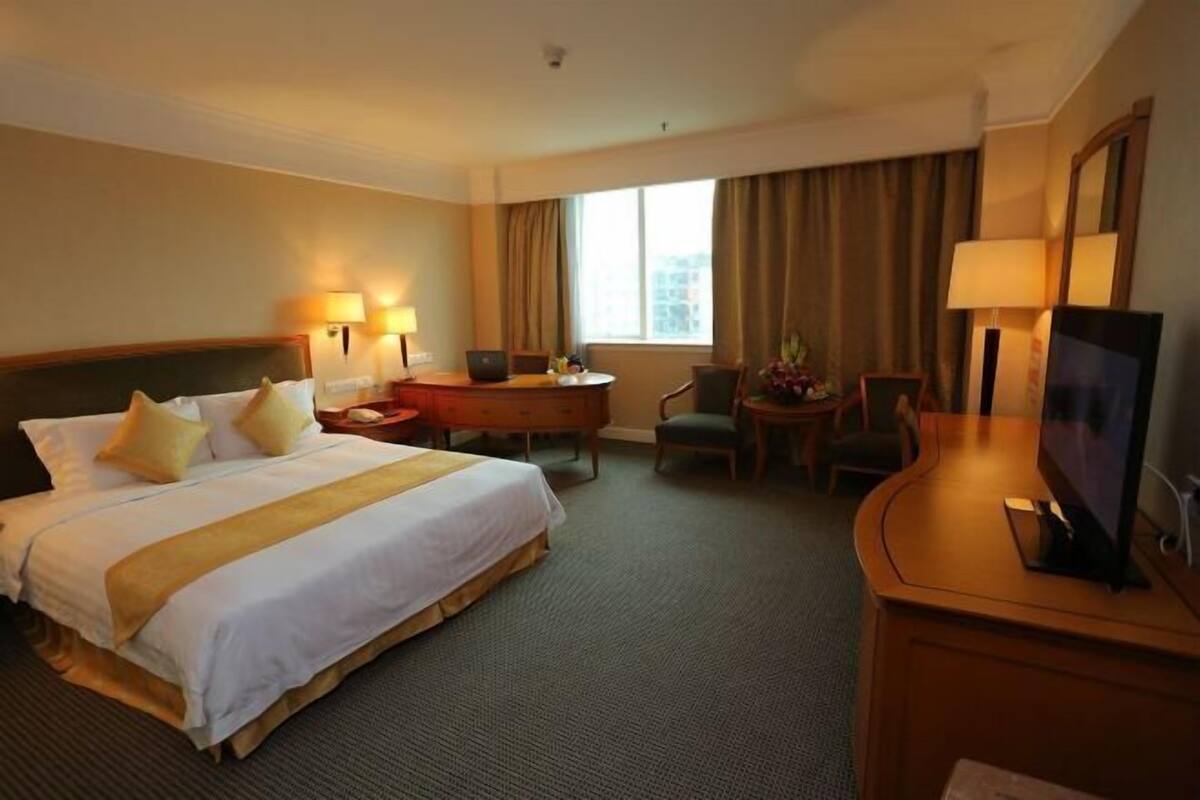 A hotel room with a large bed, a desk, a chair, a TV, and a window with curtains.
