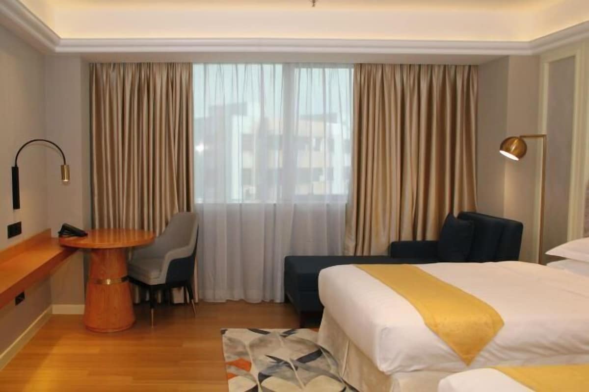 A hotel room with a bed, a desk, a chair, and a window with curtains.