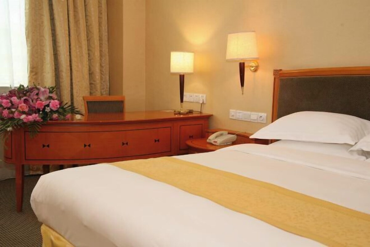 A hotel room with a bed, a wooden dresser, a telephone, and two wall-mounted lamps.