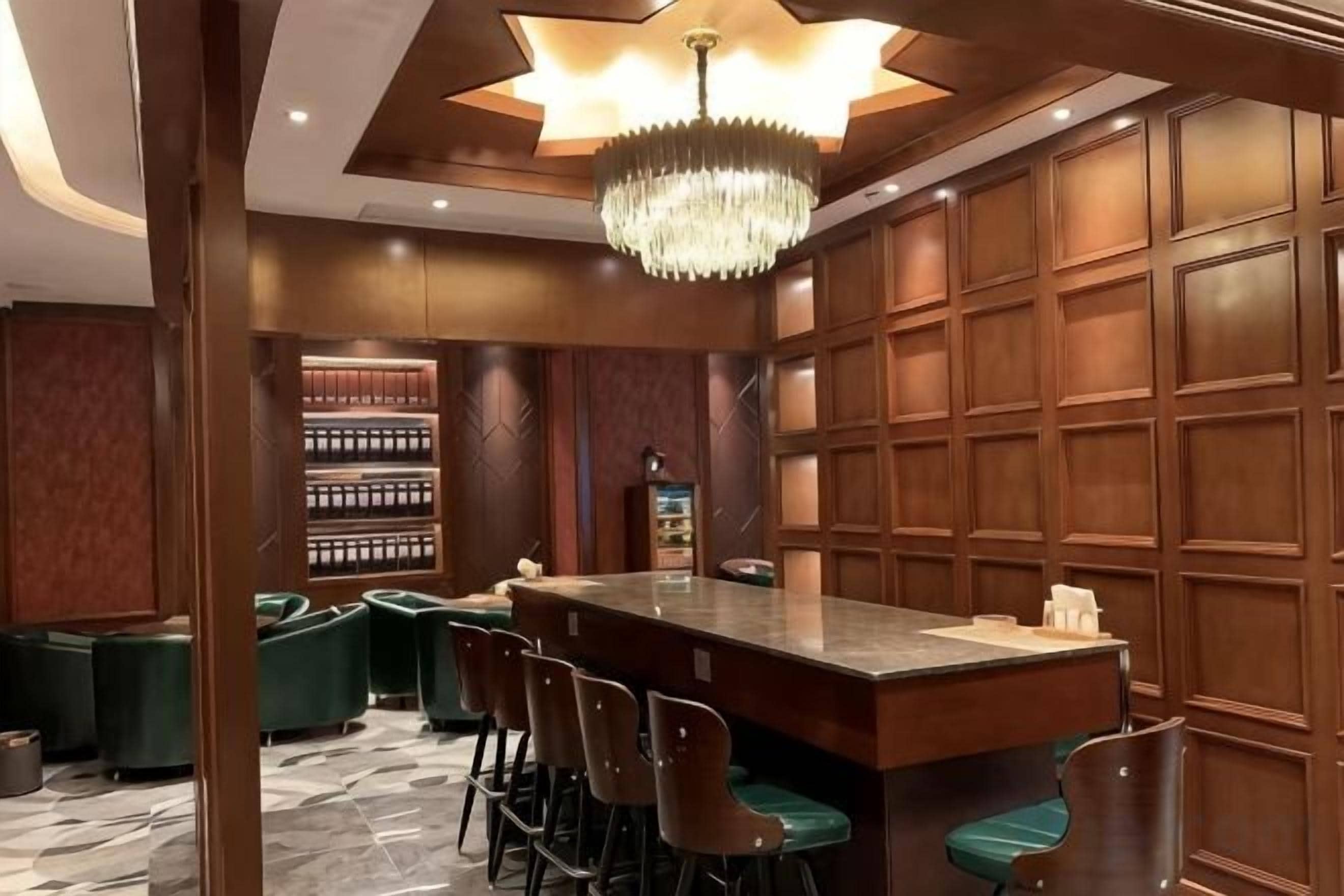 A bar area with a long counter, multiple bar stools, and a chandelier.