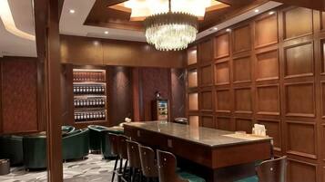 A bar area with a long counter, multiple bar stools, and a chandelier.