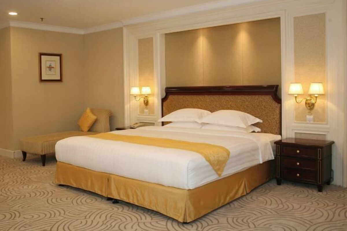 A hotel room with a large bed, two bedside tables with lamps, a bench, and a framed picture on the wall.