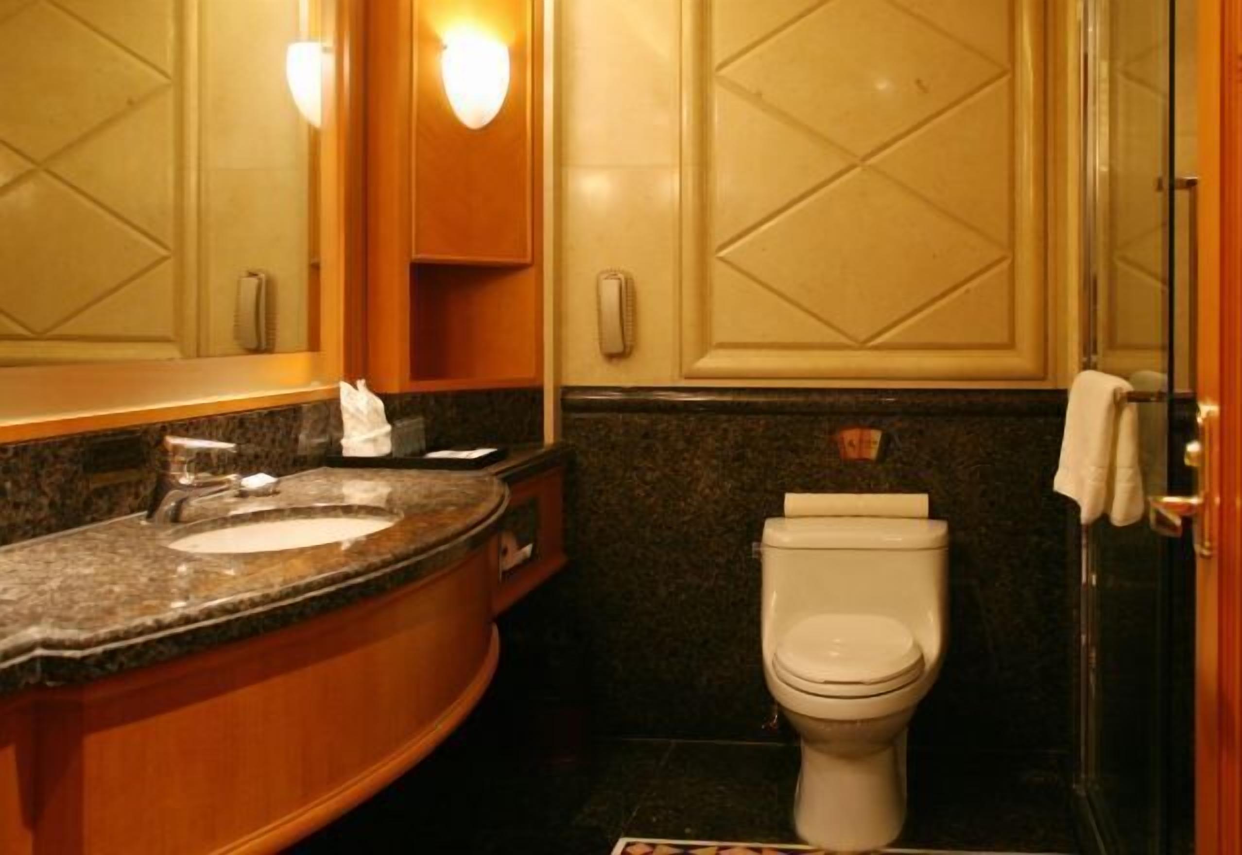 A bathroom with a granite countertop sink, a white toilet, and a mirror with wall sconces.