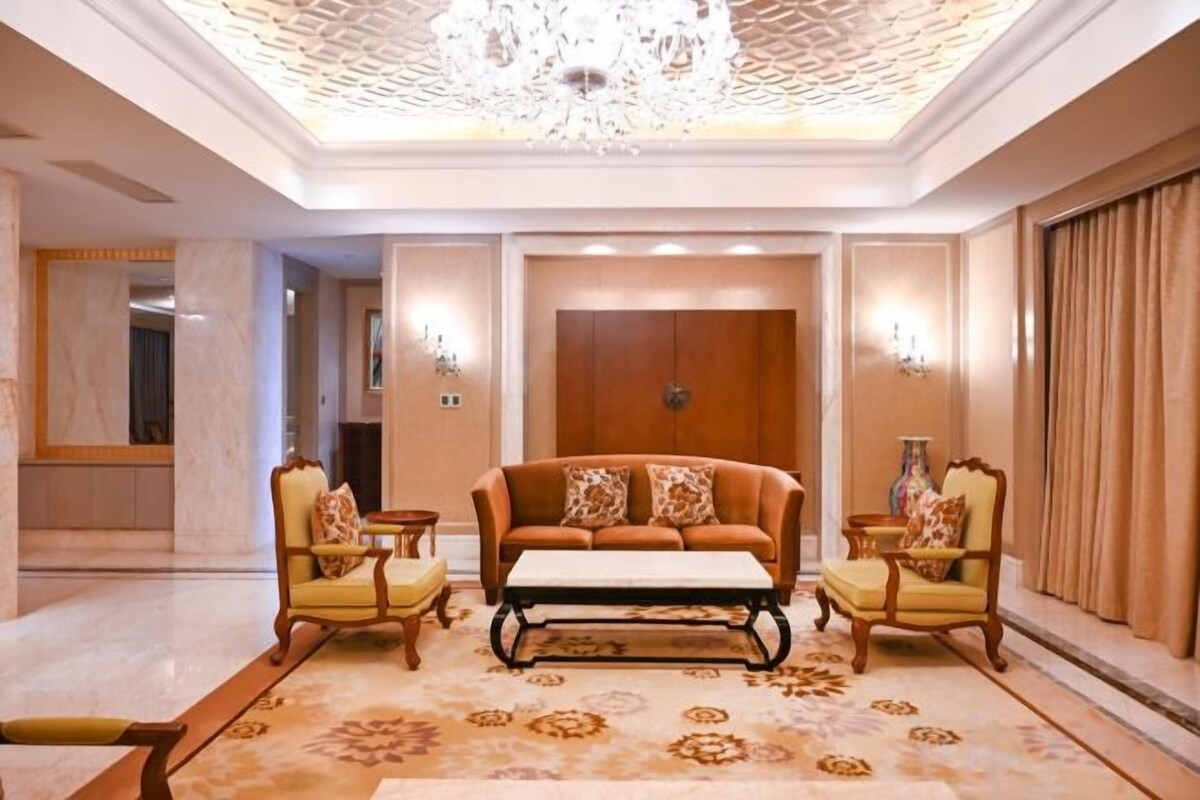 A hotel lobby with a sofa set, armchairs, a coffee table, a chandelier, and a patterned carpet.