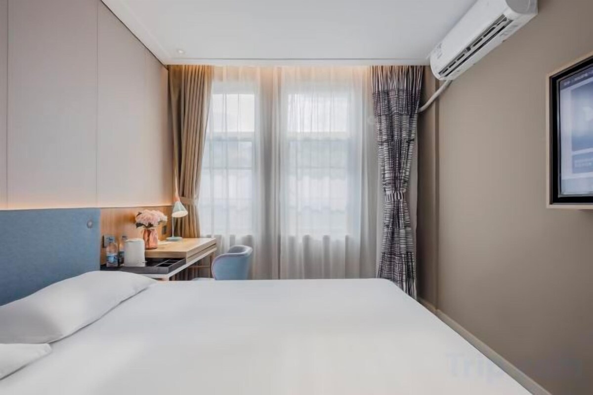 A hotel room with a bed, a desk, a chair, and an air conditioning unit.
