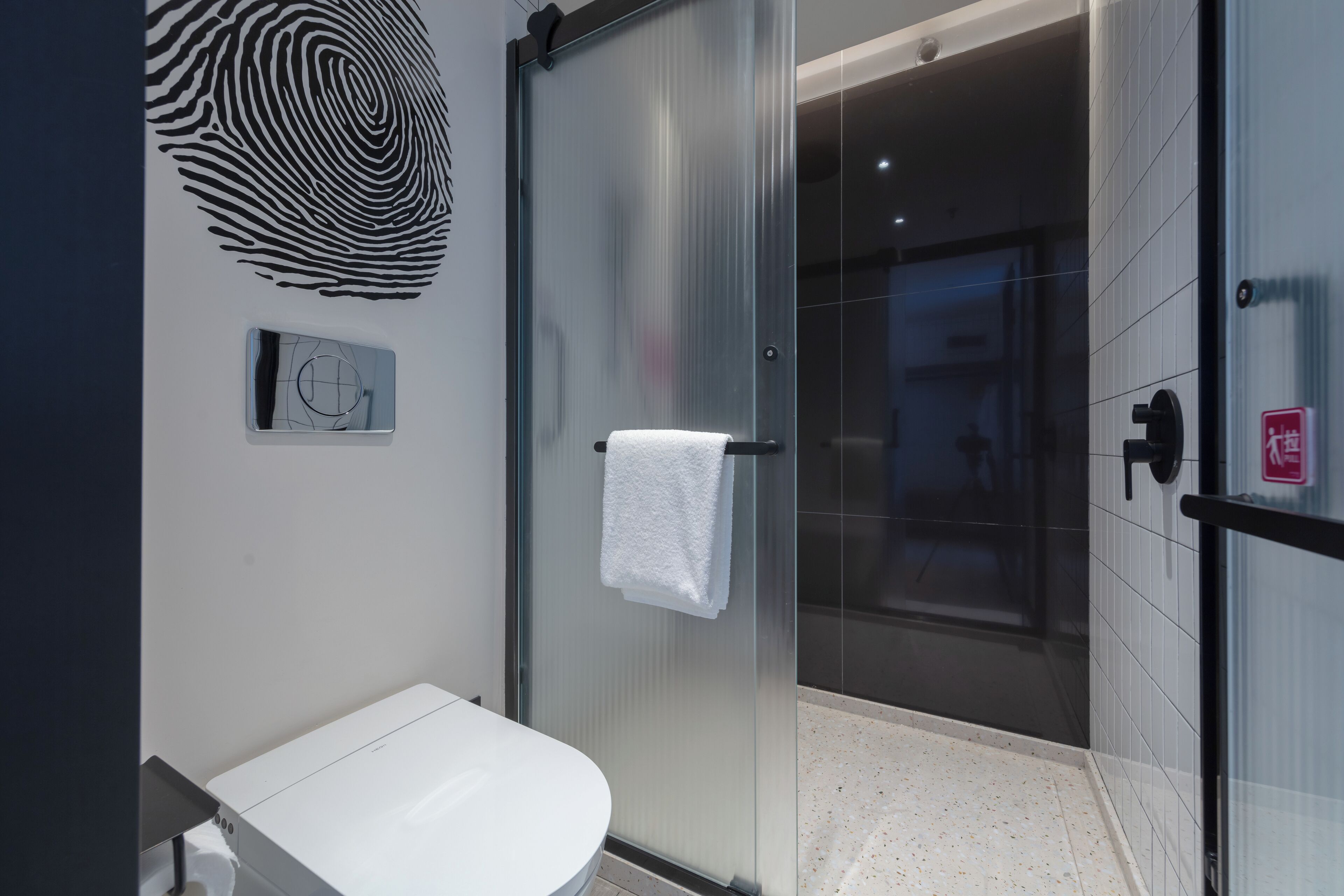 A modern bathroom with a glass shower enclosure, a white sink, and a towel hanging on the shower door.