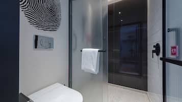 A modern bathroom with a glass shower enclosure, a white sink, and a towel hanging on the shower door.