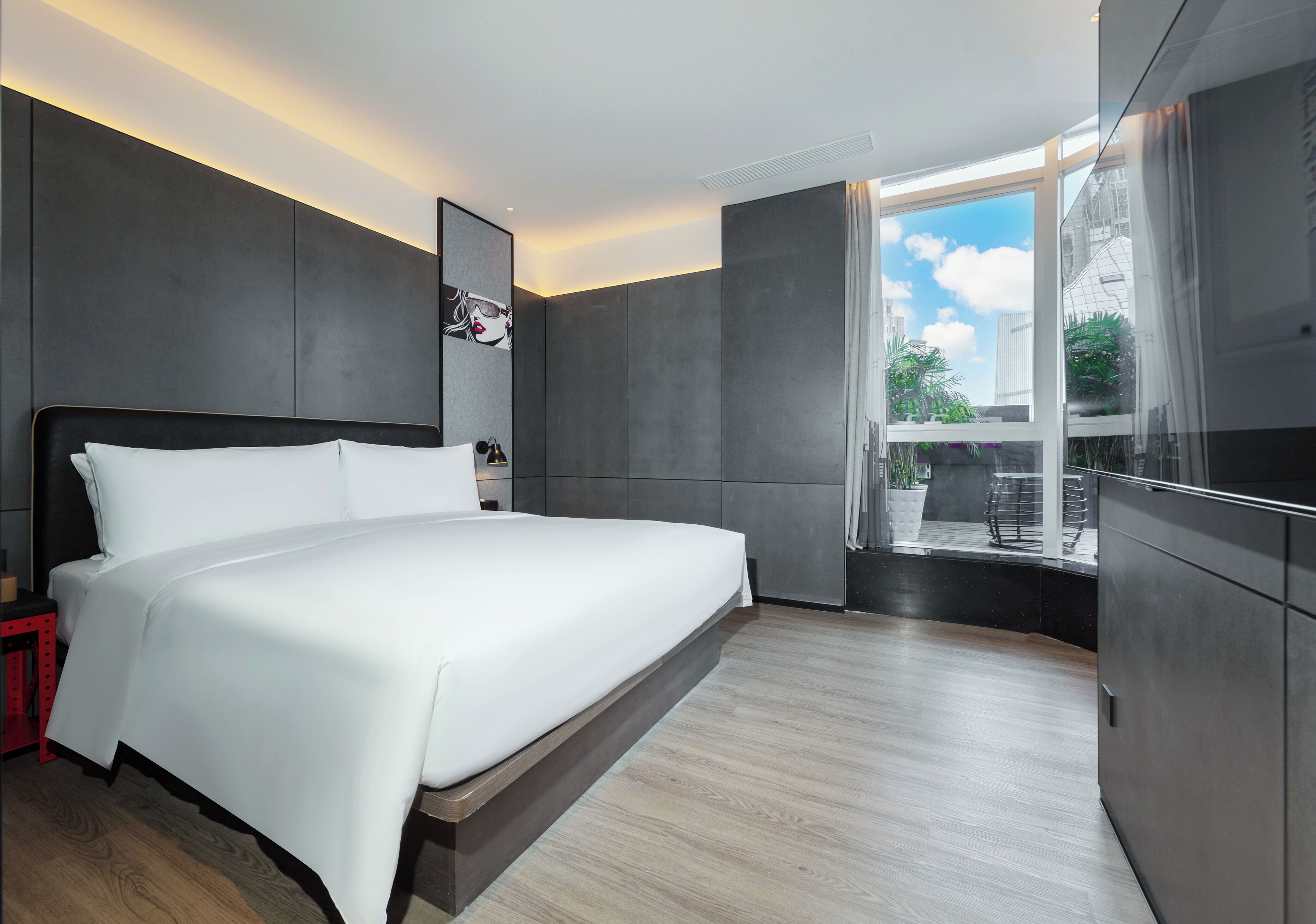 A modern hotel room with a large bed, a TV, and a view of the outdoors.